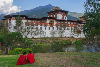 Two novice monks sit in view of the Punakha Dzong, Bhutan. This is the kingdom’s second largest and second oldest monastery fortress and a great example of the Bhutanese craftsmanship and world-class architecture