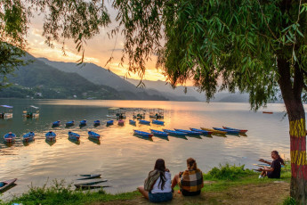 Tourists enjoy the ever changing sunset landscape over Lake Phewa, Pokhara.
Many colorful boats lay anchored on the mirror-like lake, casting dark
shadows on the water. © Kabir Uddin