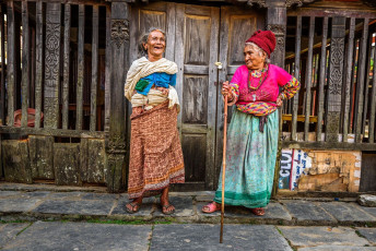 Two elderly women share a laugh on a street in Bandipur with a beautiful
wooden building in the background. © miroslav_1