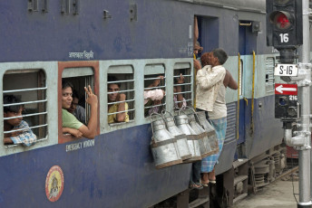 A few men hang from the door of a moving train and milk churns hang on the windows on a railway line in India © JeremyRichards