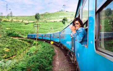 A smiling tourist enjoys the picturesque train journey to Nuwara Eliya, traveling through tea plantations and green fields, Sri Lanka ©solovyova