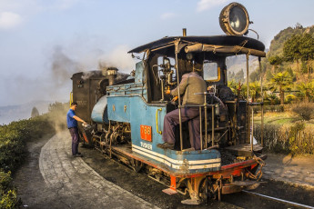 A Toy Train takes a hold on the historic Darjeeling Himalayan Railway during a stopover while the driver lubricates the engine with oil, Darjeeling, India. © Anandoart