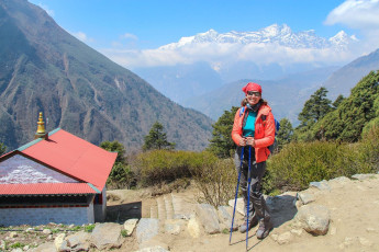 A female trekker with her daypack smiles at the camera after arriving at the entrance to Thyangboche village in the Himalayan Mountains in Nepal. In the background the Kongde Ri Mountains, one of the more difficult peaks to climb, can be seen © Andrey Rykov