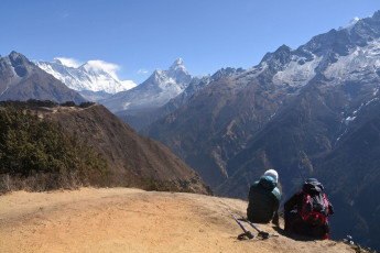 A couple of trekkers relax to catch their breath and to enjoy the magnificent view of Mount Everest in the distance, Khumjung © Alexander Jung