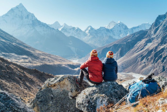 Discarding their daypacks and walking poles for a while, two trekker sit down to admire the amazing valley views with the 22,349 ft./6812 m-high Ama Dablam and 21,309 ft./6495 m-high Tobuche Peaks in the distance. The picture was taken outside Dughla, a small hamlet south of the Khumbu Glacier © Solovyova