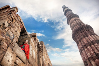 A visitor looks at the Qutub Minar or Victory Tower in the Qutub Mosque Complex in Old Delhi. The surface of the tower is elaborately decorated with geometric patterns and inscriptions from the Quran © Pikoso.kz