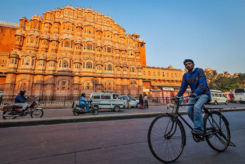 A distant view of grand Hawa Mahal Palace, also known as “ the palace of winds” where a local man rides his bicycle and explores the city of Jaipur, Rajasthan, India. © f9photos
