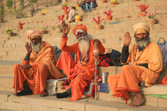 Three ascetics in their traditional dress wave at the camera from the steps of the ghats of the river Ganges in Varanasi, India © Mark Dozier