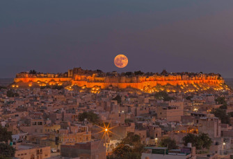 Spectacular sight of the full moon rising above Jaisalmer Fort, Rajasthan, with the city at its feet. Unlike most other forts in India, this is a living complex with hotels, shops and houses inside its walls