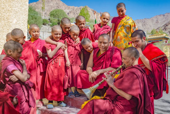 Young novices in striking shades of red watch a monk playing his traditional Tibetan flute at the monastery of Likir, Leh © chris piason