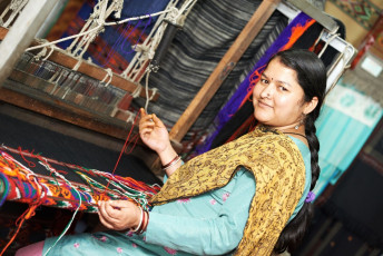 A young Nepalese woman smiles for a picture while weaving a colorful woolen scarf on a handloom in Nepal © Dmitry Kalinovsky