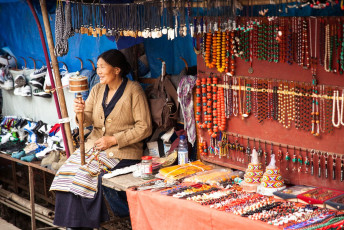 A Tibetan lady next to her display of jewelry in a street market in Dharamsala. In her hand she holds a traditional prayer wheel, Himachal Pradesh © Elena Ermakova