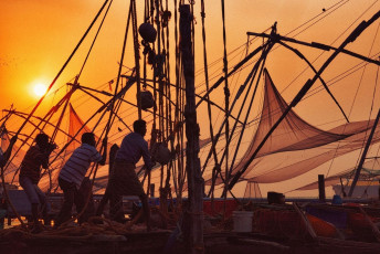 A group of men lined up to fetch Chinese fishing nets at the glowing time of sunset in Kochi, Kerala, India. Chinese Fishing Nets were introduced to the fishermen in Kochi over 500 years ago © powerofforeeve