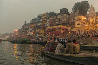A boat trip with passengers takes place along the beautiful Ghats of Varanasi at sunset, India. © helovi