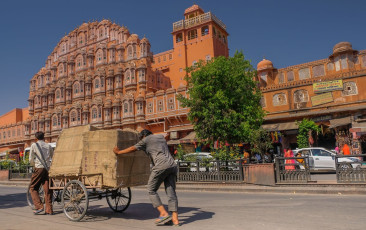 Two vendors push their produce past the Palace of the Winds, Jaipur. A total of 953 lattice screens windows adorn the façade. The palace’s distinctive pink color comes from the natural sandstone with which it was built - Photo By  The Life in Pics