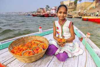 A charming little girl sitting on a boat, sells flowers and candles amidst the Ganges River at Varanasi, India. © Bartosz Hadyniak