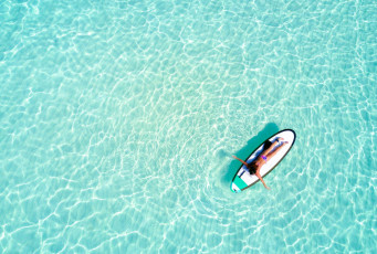 The sea water at the Maldives is famous for its beautiful aquamarine color. In this aerial view a woman relaxes on a surfboard © Sven Hansche