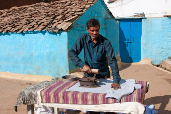 A scene of rural India wherein a man is ironing the laundry with an old and rusty iron against a background of blue colored huts in a village in Madhya Pradesh, India. © Radiokafka