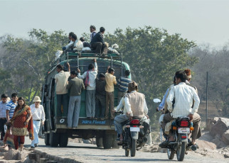 An overloaded bus on the road with people sitting on the roof and hanging in the back transports them to their desired place, Madhya Pradesh, India. © Claudine Van Massenhove