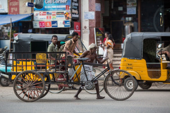 A rickshaw driver pushes his rickshaw with two travelers on it along the road of Madurai, Tamil Nadu. © sergemi