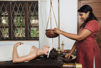 A woman relaxing and taking an Ayurveda Shirodhara rejuvenation treatment which is a powerful ayurvedic therapy that stabilizes and balances the mind and body in Kerala, India. © Nina Lishchuk