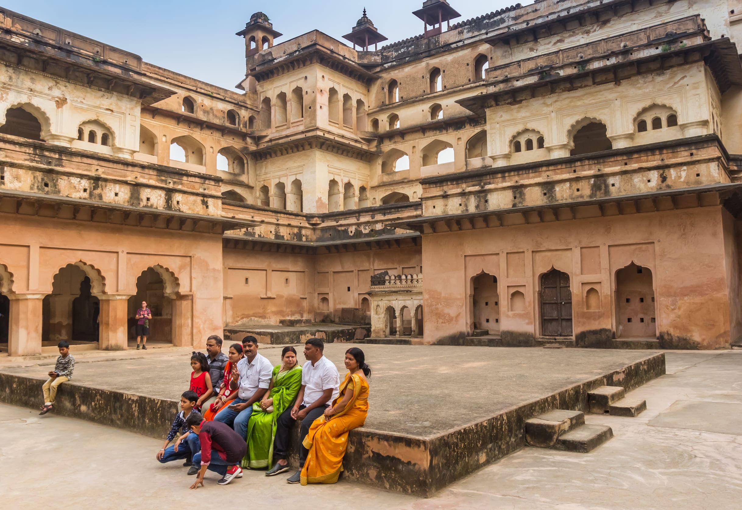A family sitting in the courtyard of Raj Mahal, situated in Orchha, and posing for a group photograph