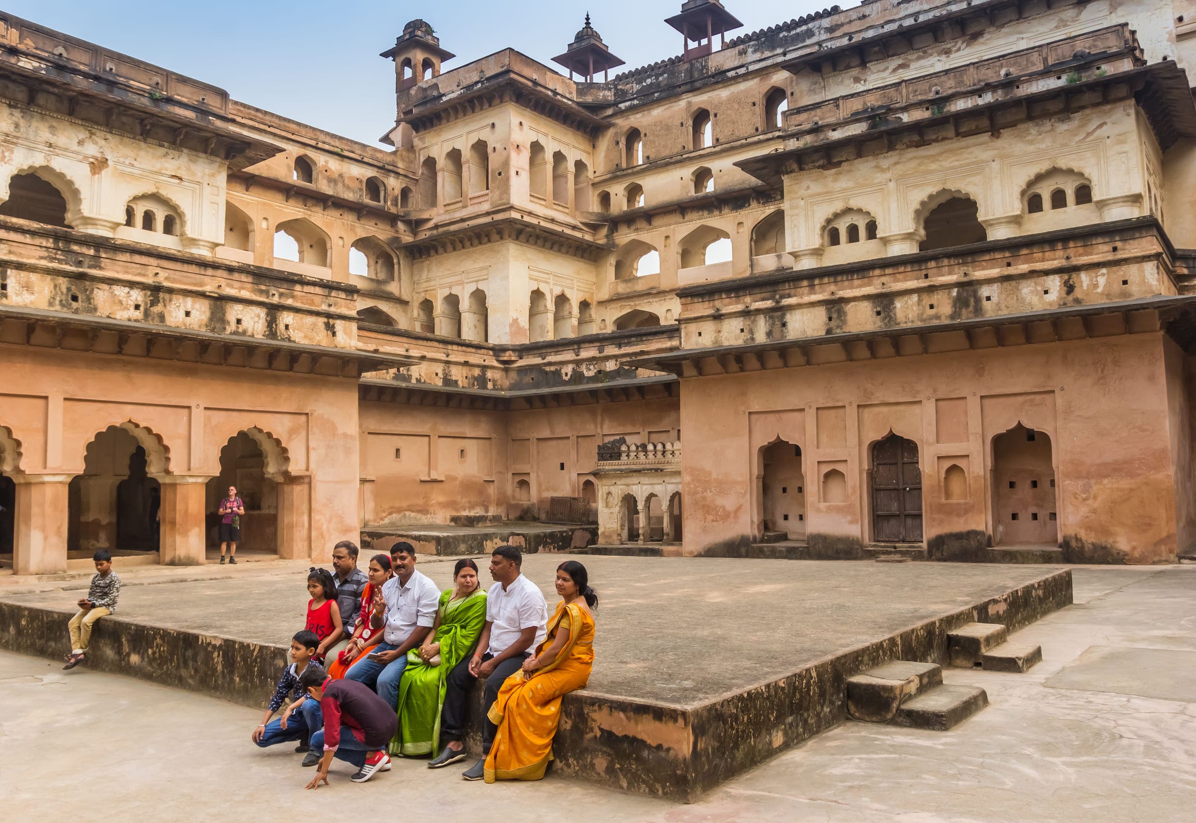 A family sitting in the courtyard of Raj Mahal, situated in Orchha, and posing for a group photograph 