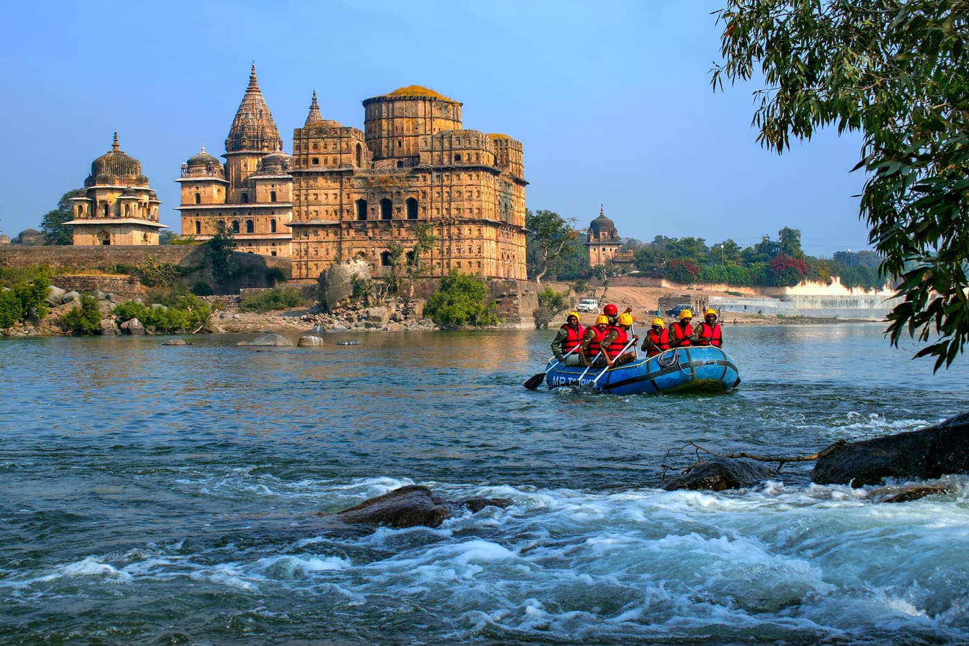 A group of tourists enjoying water rafting on the rapids of the Betwa river and the amazing sights of Orchha from a different angle 