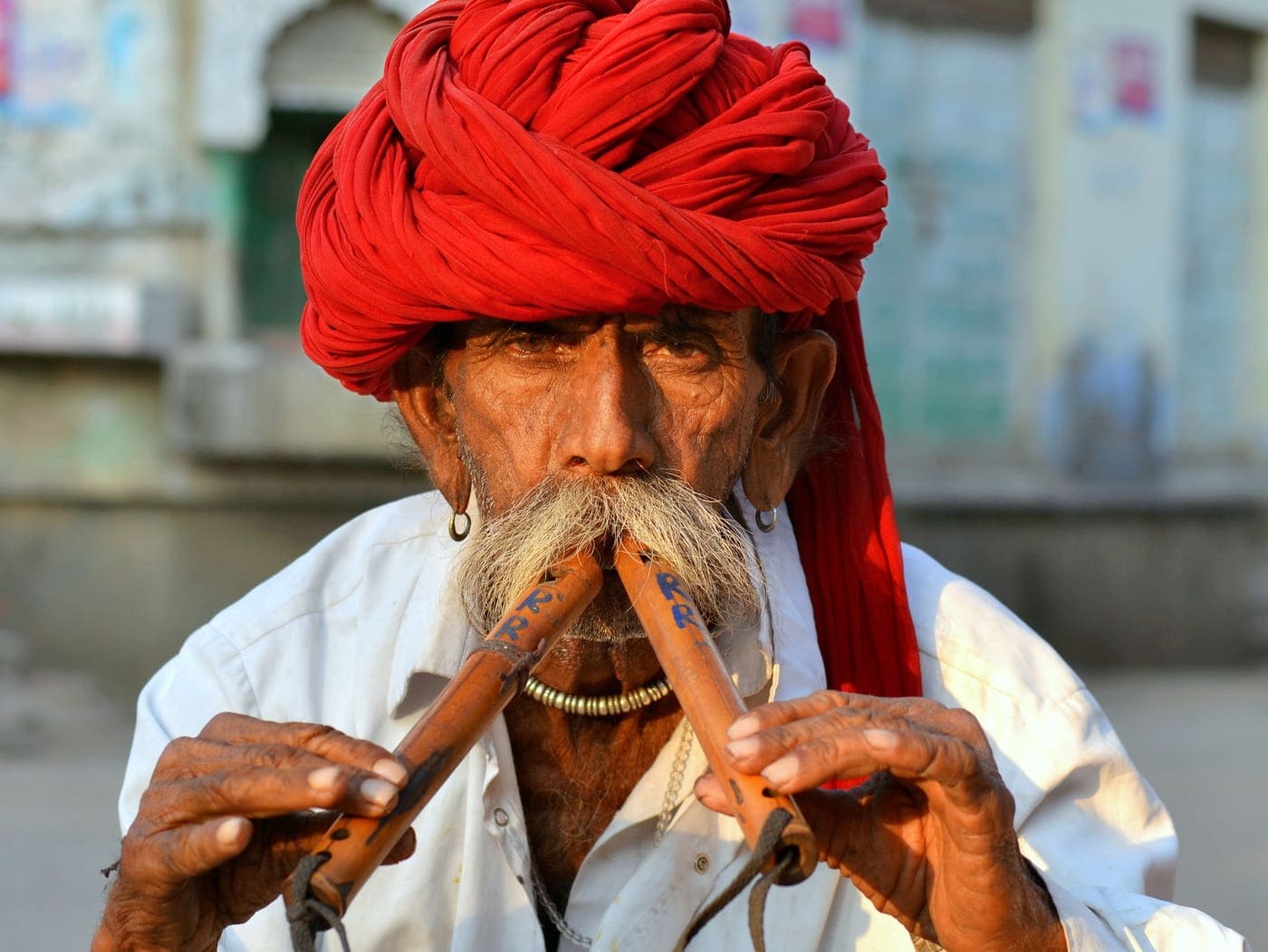 A mustached man playing jheeka, a rectangular Indian tambourine, and singing at Ram Raja Mandir in Orchha 