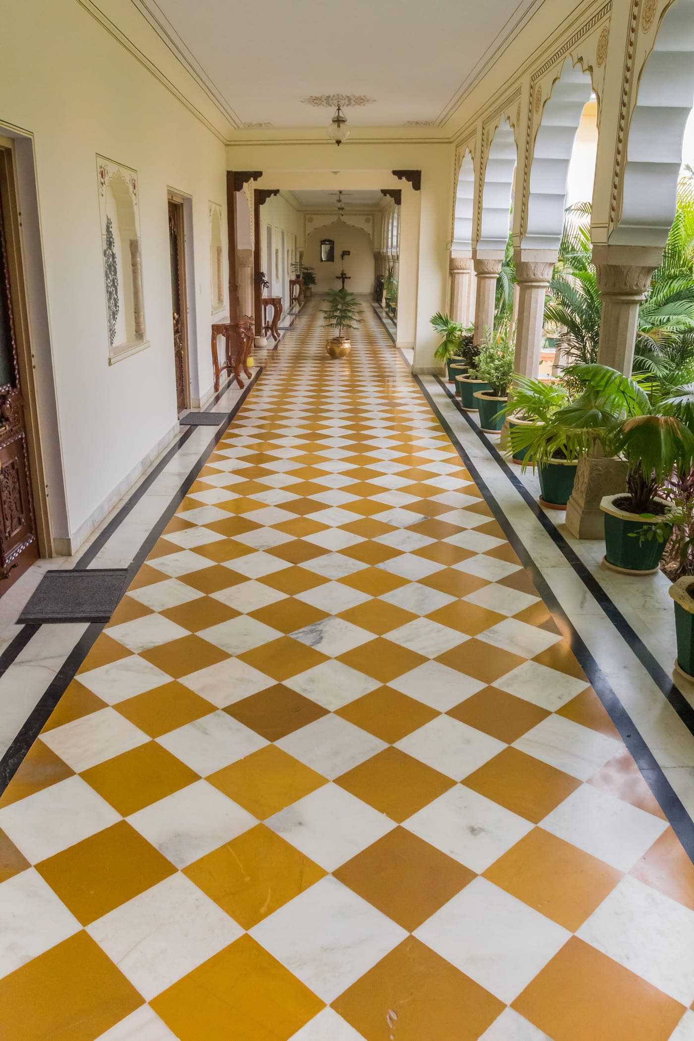 A yellow and white chequered corridor of a heritage hotel in Orchha lined with beautiful Areca Palm planters 