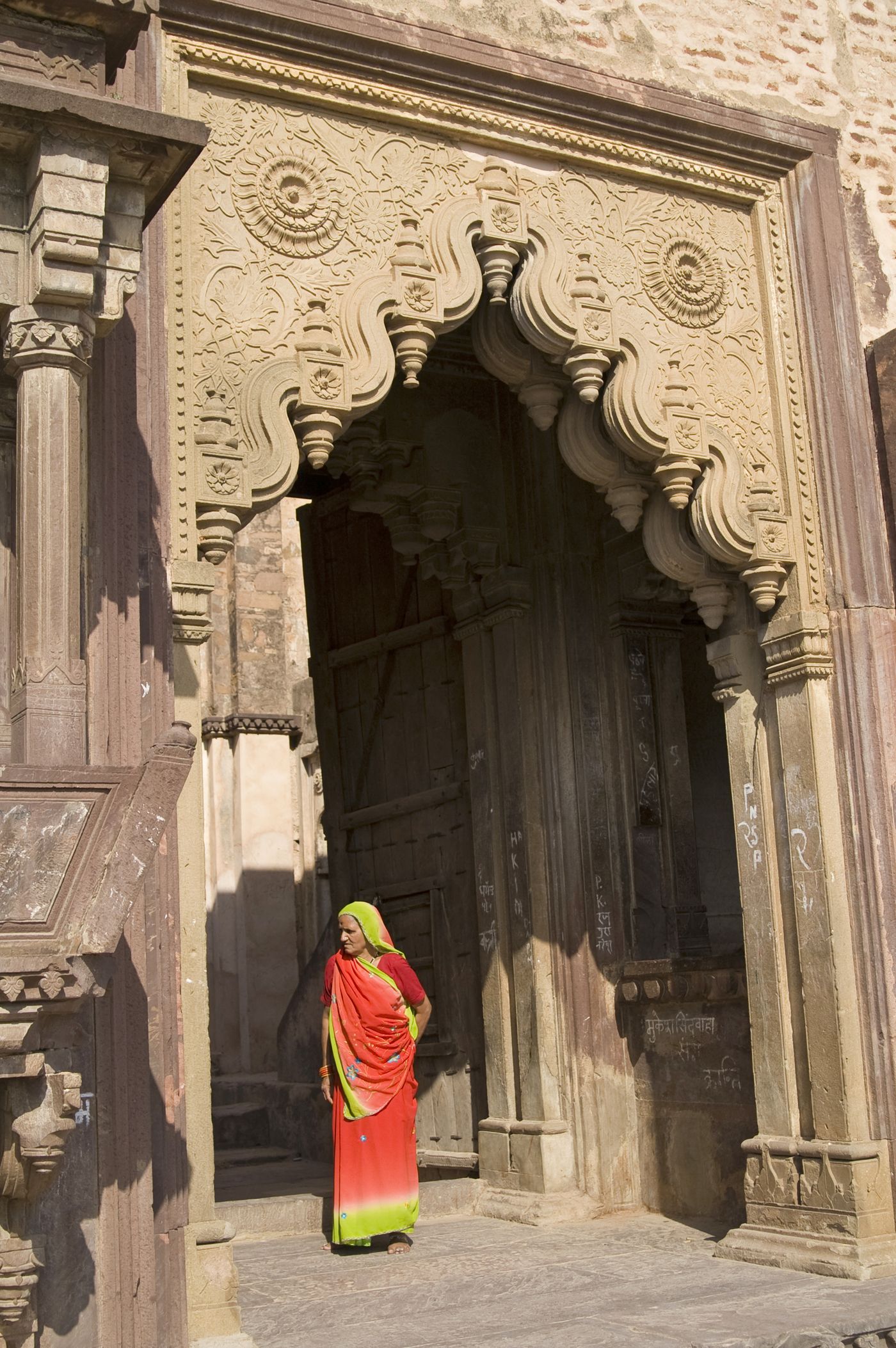 An Indian lady wearing an orange saree, the traditional attire of women in India, leaving a temple in Orchha. Most ancient temples in Orchha were built hundreds of years ago and are still pretty popular 