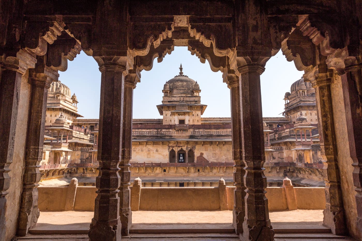 The structure of the regal Jahangir Palace, also known as the Orchha Palace peeks through the carved pillars 