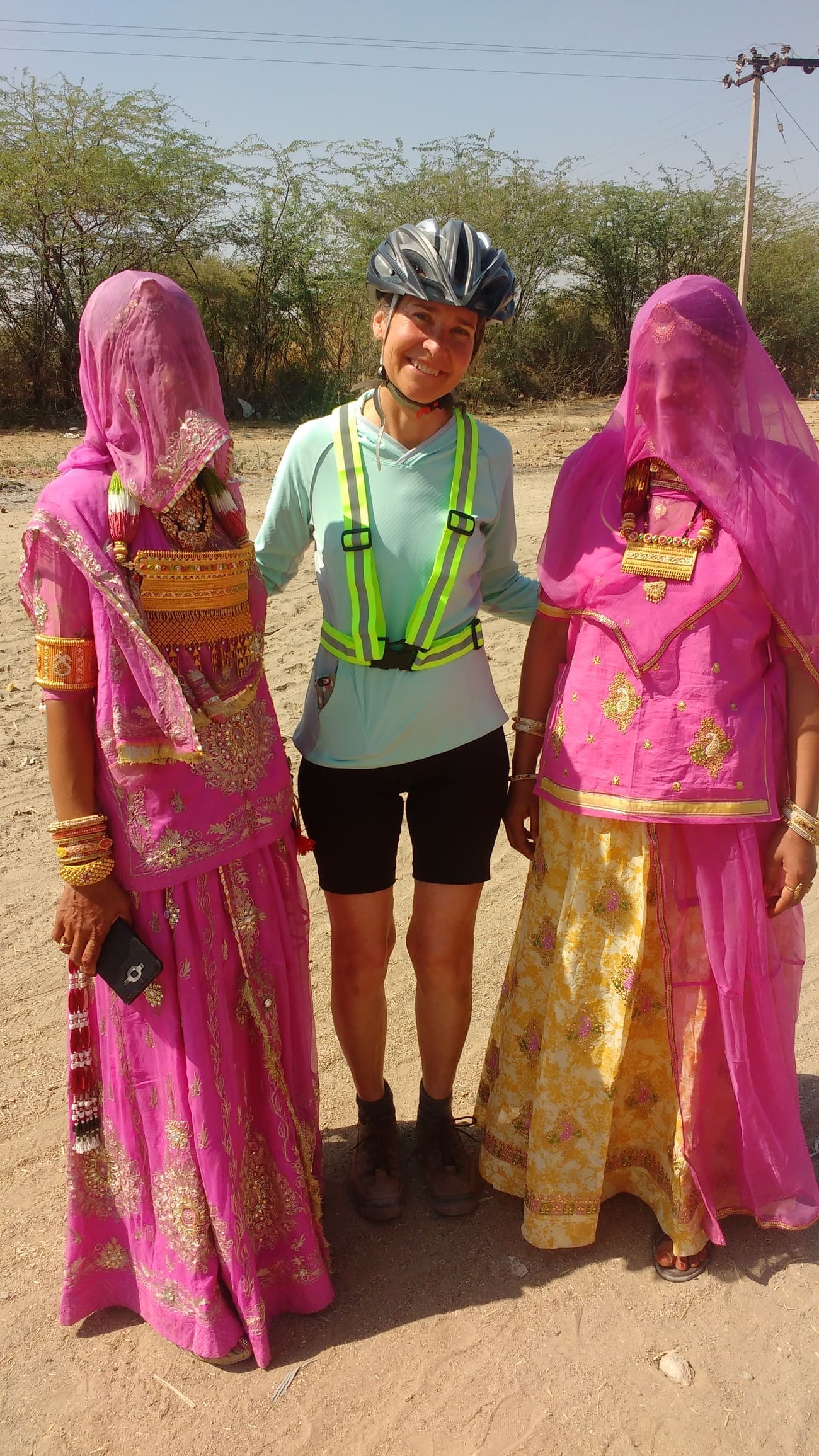 A cyclist posing with two local ladies beautifully dressed in pink and gold