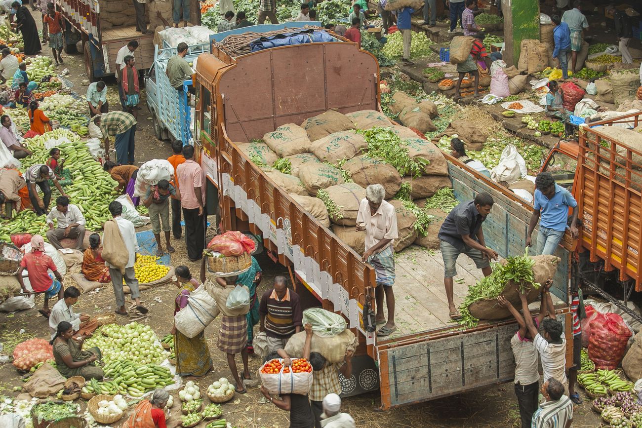 A huge number of laborers empty out sacks from a truck carrying produce, while vendors sell vegetables down below on the street of Bangalore 