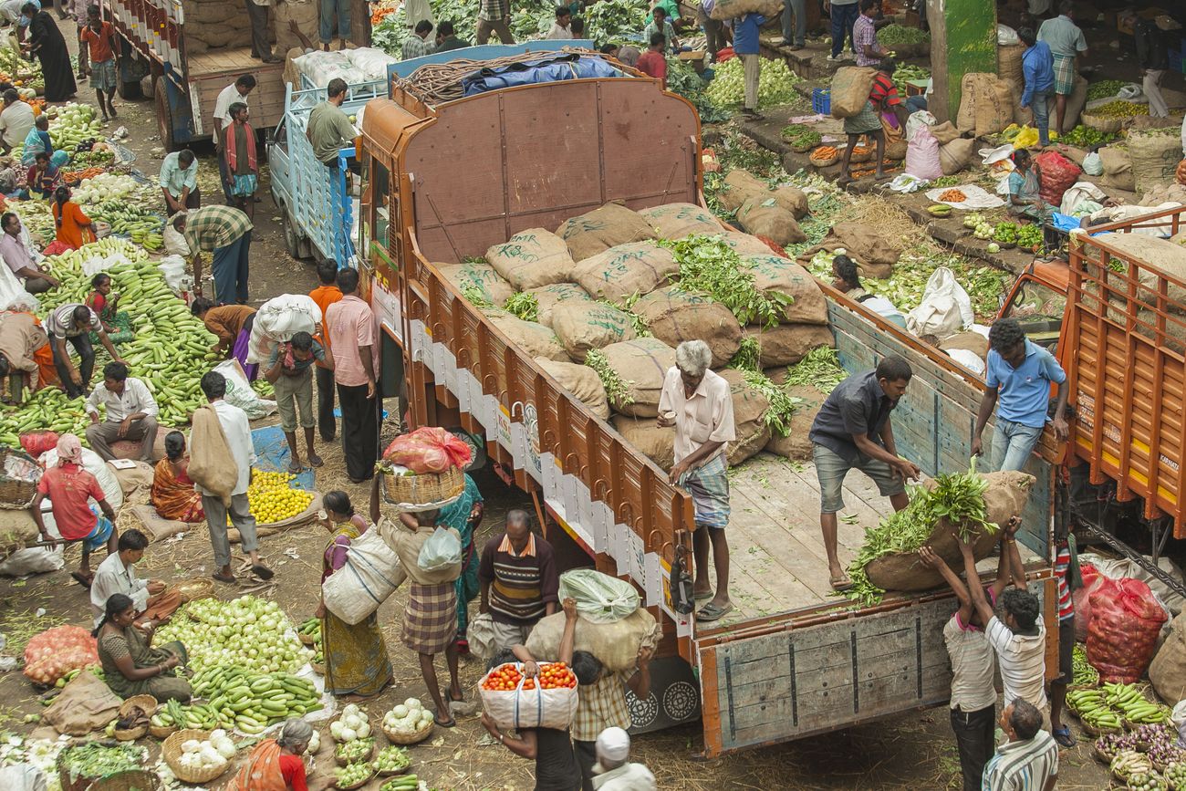 A huge number of laborers empty out sacks from a truck carrying produce, while vendors sell vegetables down below on the street of Bangalore