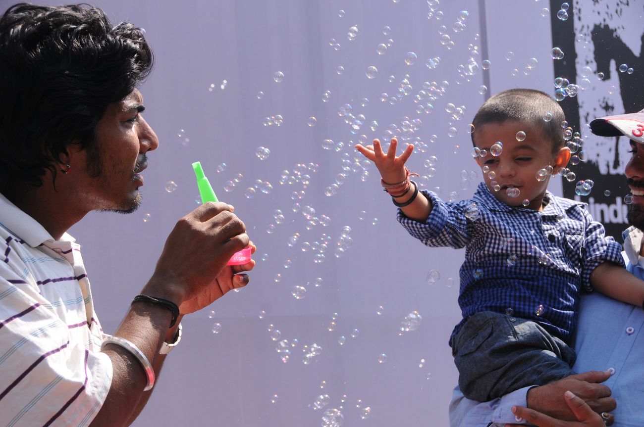 A street vendor shows how to blow bubbles to a child who then enjoys it with his hands during the Kala Ghoda Arts Festival in Mumbai 
