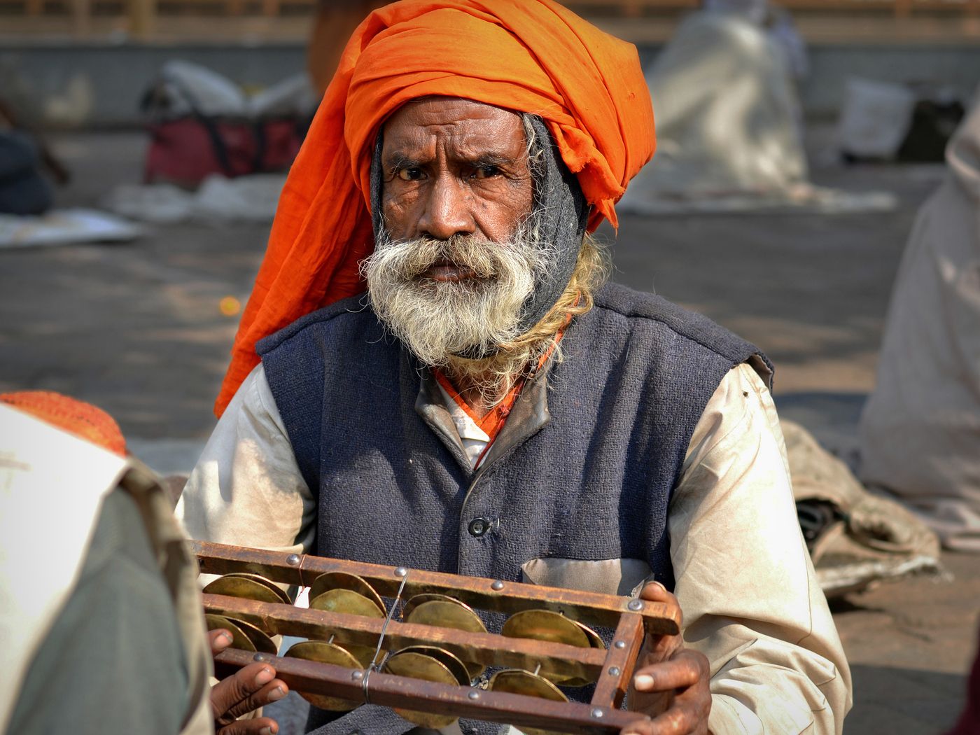 An old Indian man with a white beard, wearing a saffron turban and playing a traditional musical instrument outside the Ram Raja temple in Orchhan