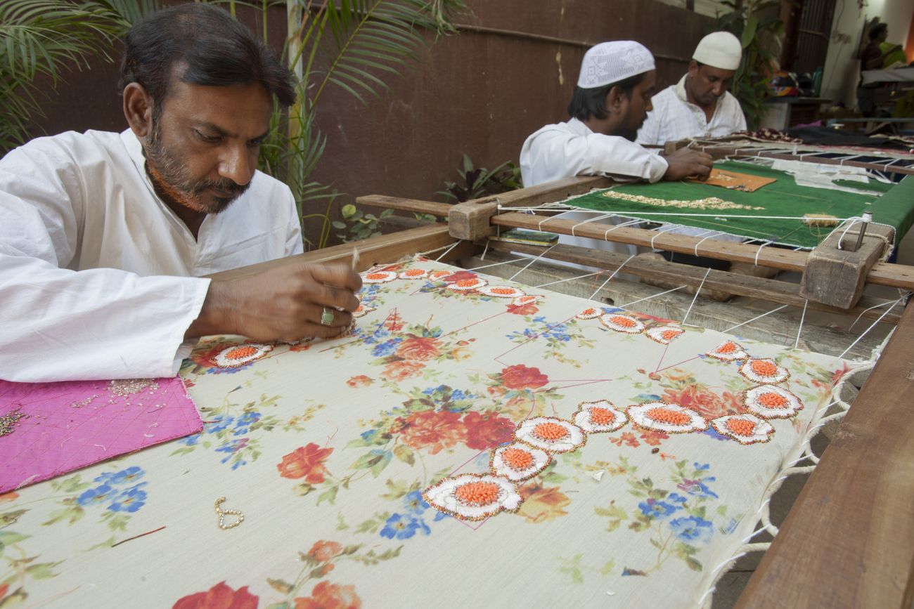 Three Muslim craftsmen do embroidery work on pieces of clothes in the traditional and beautiful method of India 
