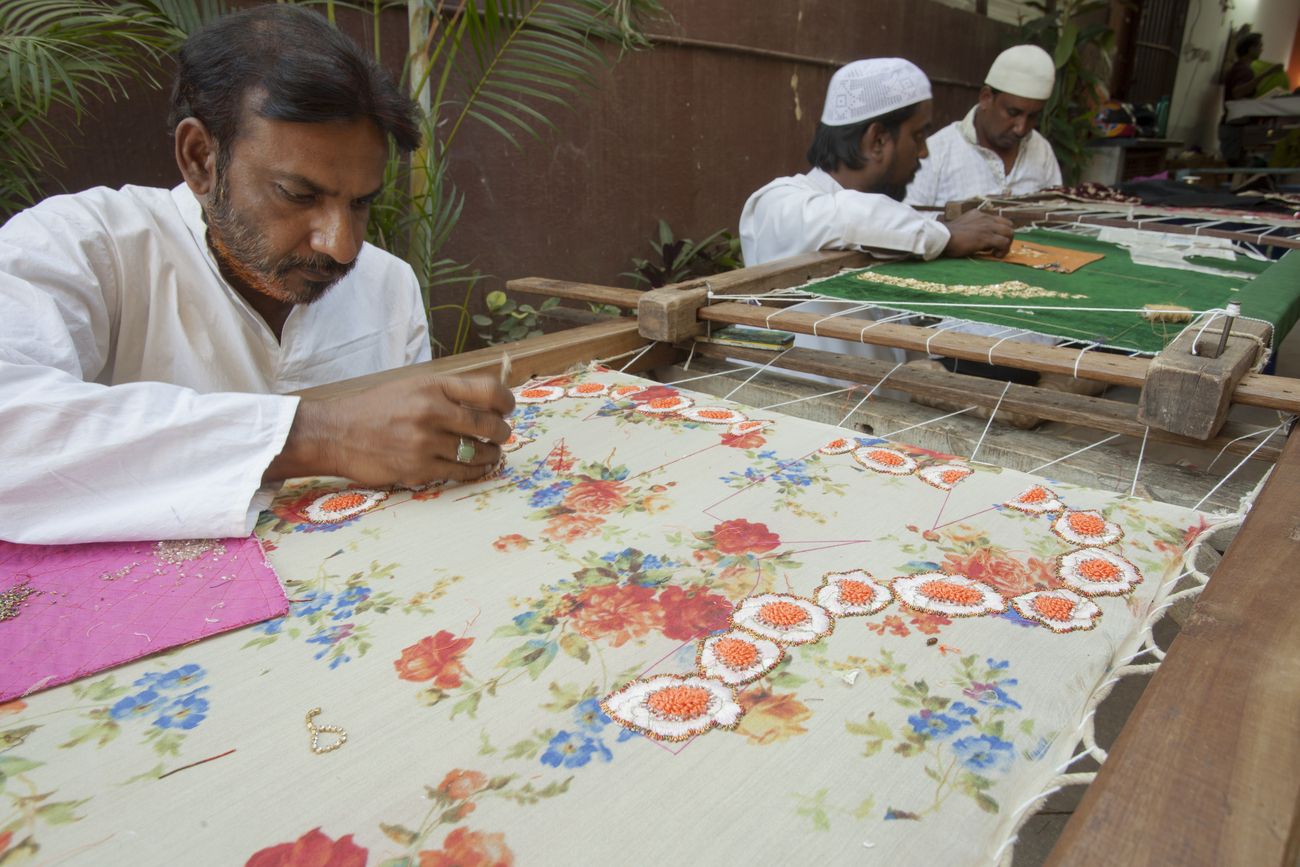 Three Muslim craftsmen do embroidery work on pieces of clothes in the traditional and beautiful method of India