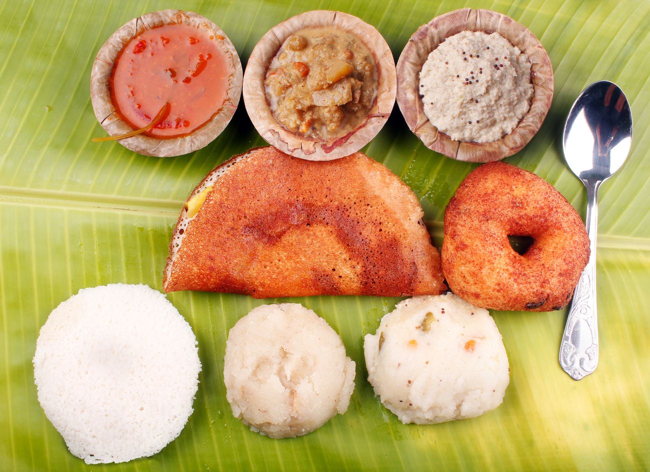 Traditional south Indian breakfasts with a platter including dosa, idli, vada, upma, kesari bath with spicy Indian curry and chutney served on a banana leaf 