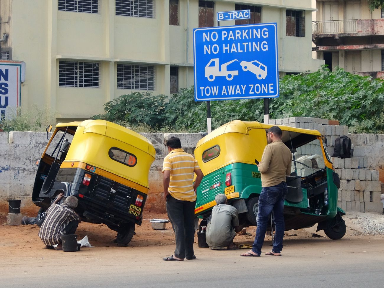 Two Taxi drivers repair their auto-rickshaws, commonly known as tuk-tuk while the travelers wait on the street of Bangalore 