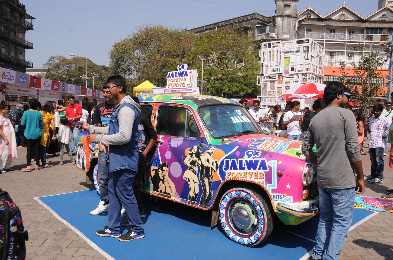 People and visitors get their pictures clicked while standing in front of a hand painted colorful decorated car during the Kala Ghoda Arts Festival 