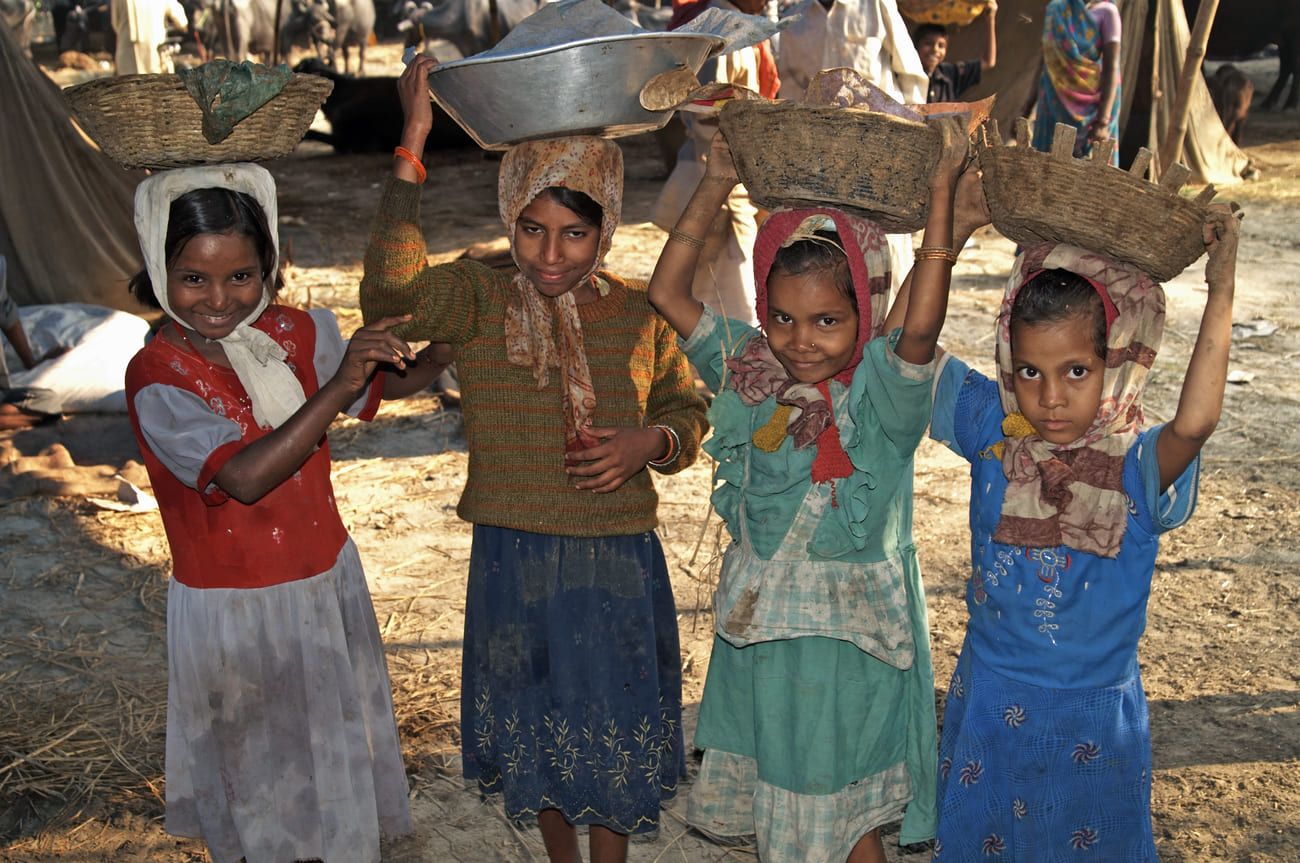 A bunch of smiling children carrying buckets of manure collected during the Sonepur Cattle Fair on their heads