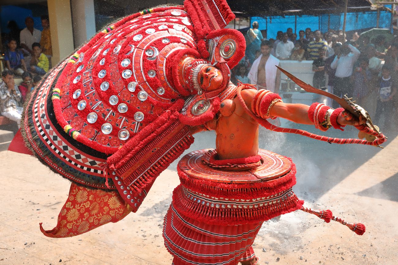 a dancer with red headgear performing theyyam