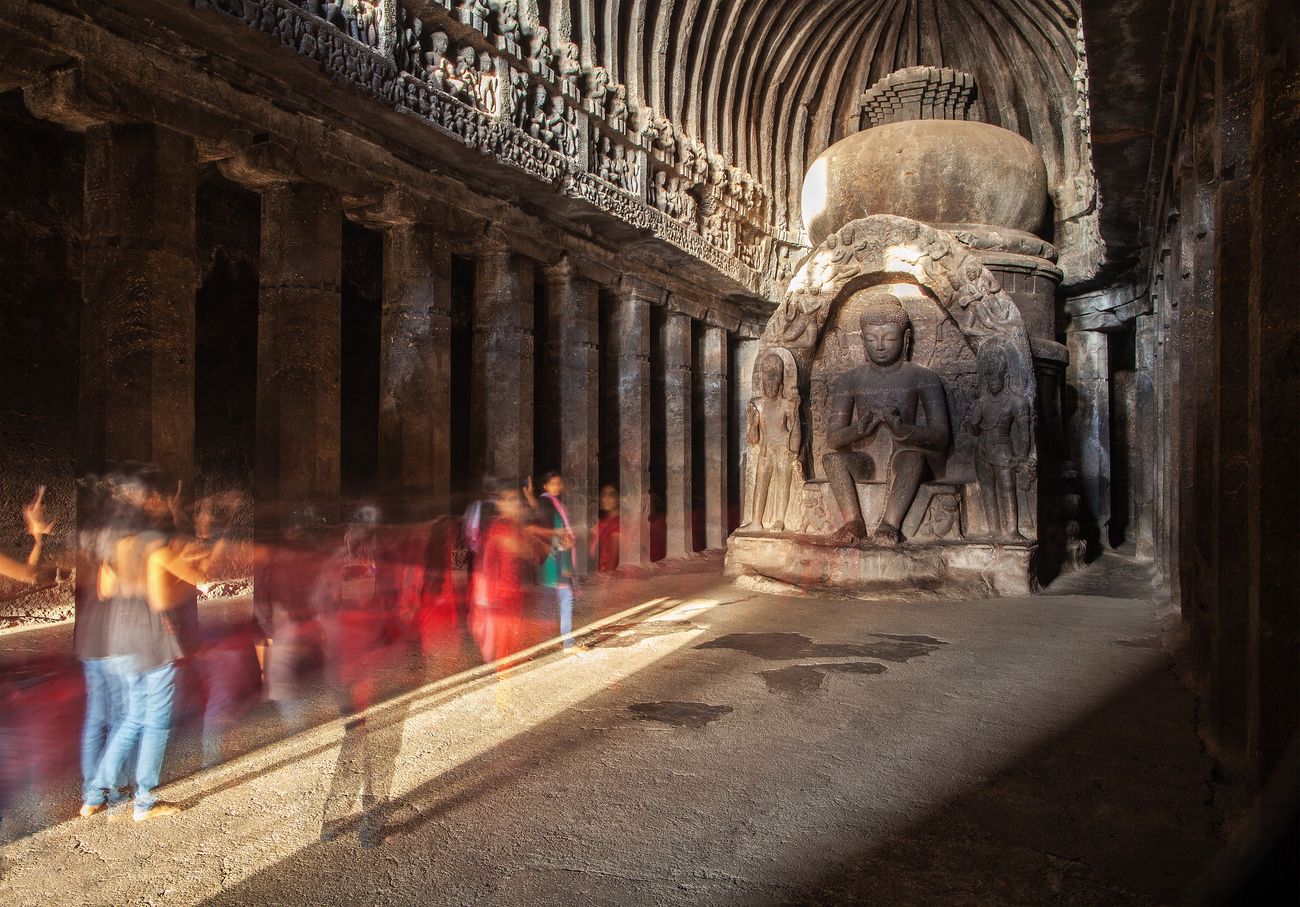 A group of tourists shot with long exposure as they visit a stone carved statue of the Buddha sitting in sunlight 