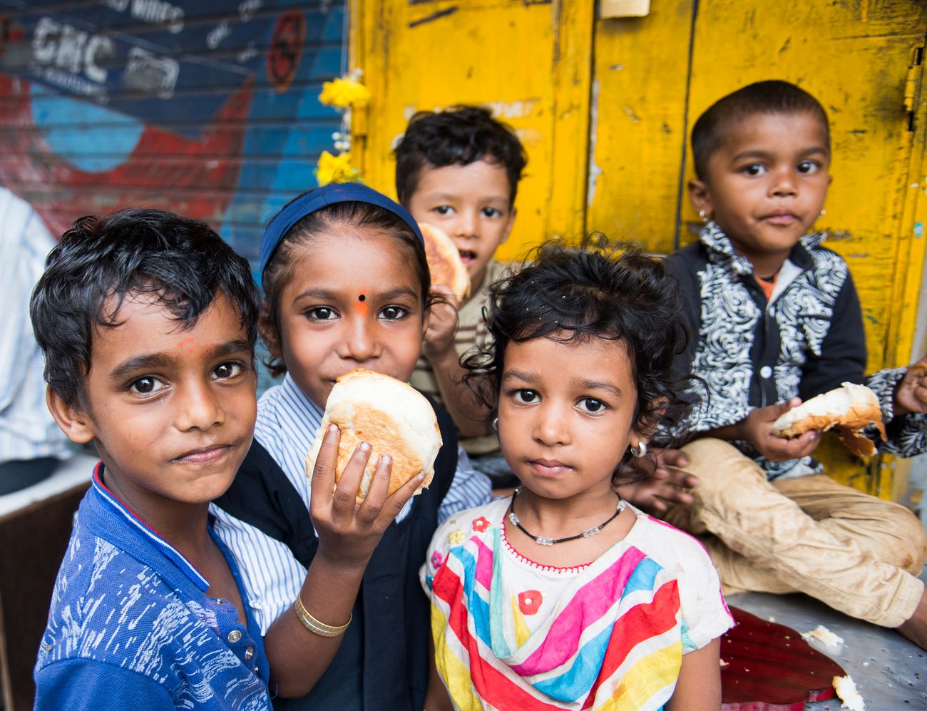 A group of young kids look into the camera while eating sweet bread from a roadside shop