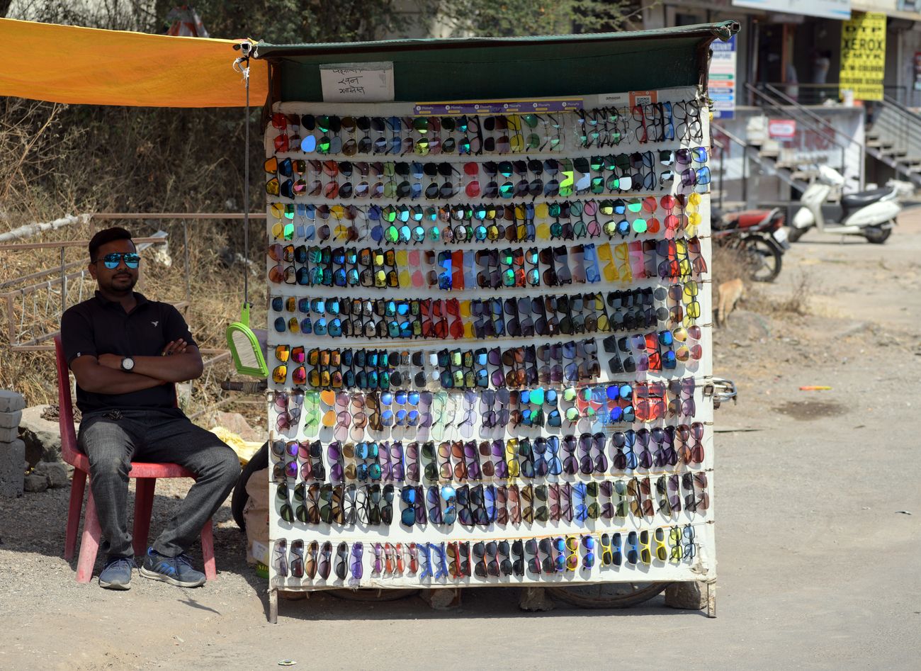 A man uses a pair of sunglasses from his roadside trading store to protect his eyes from the glare of the sun