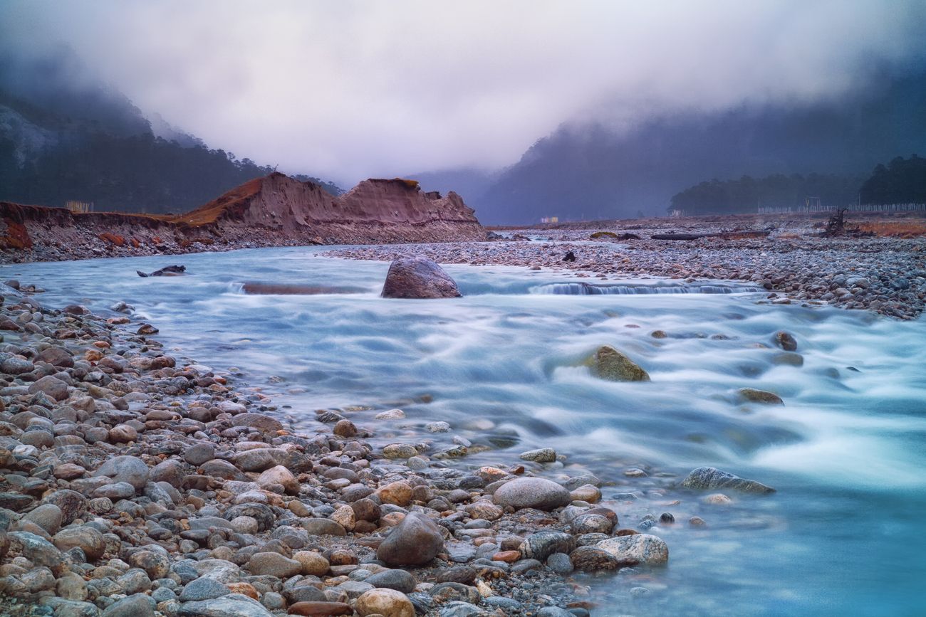 A mountain river flows through the Natural Reserve in the Kanchenjunga area while misty clouds cover the peaks of the mountains