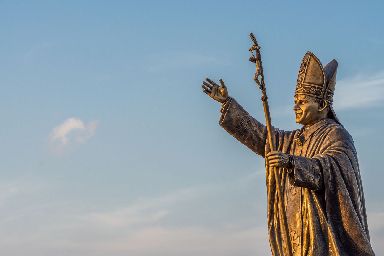 A smiling Pope John Paul ll is illuminated in gold against the blue sky at the St. Thomas Mount National Shrine