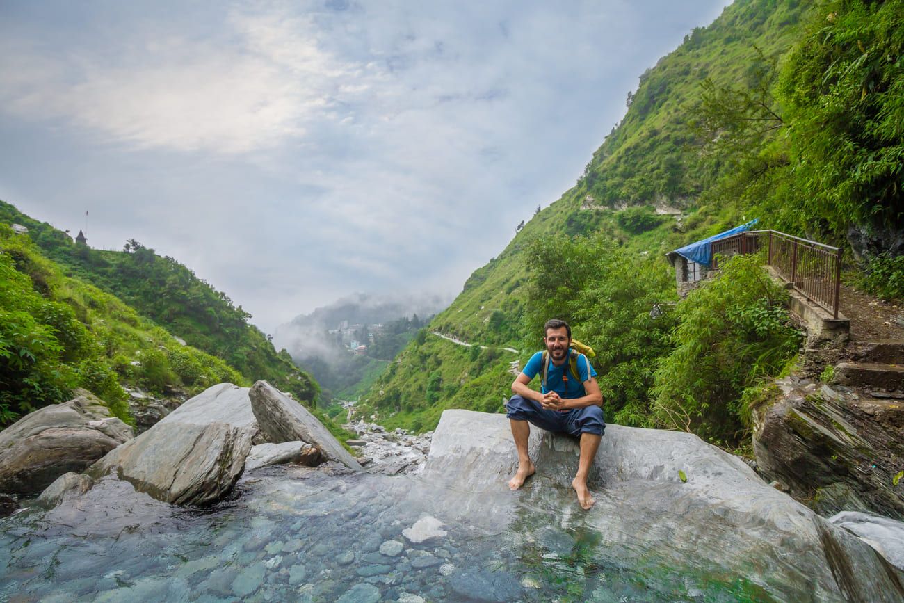 A tourist takes a selfie at Bhagsunag Waterfall surrounded by lush green mountains 